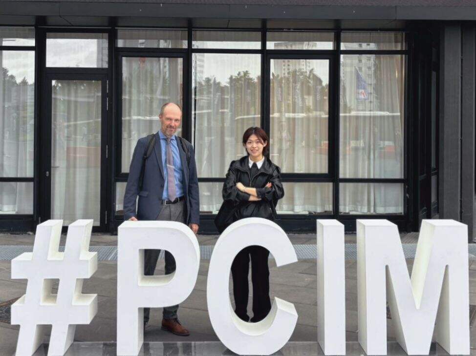 Two professionals pose in front of large white '#PCIM' letters outside a modern glass building.